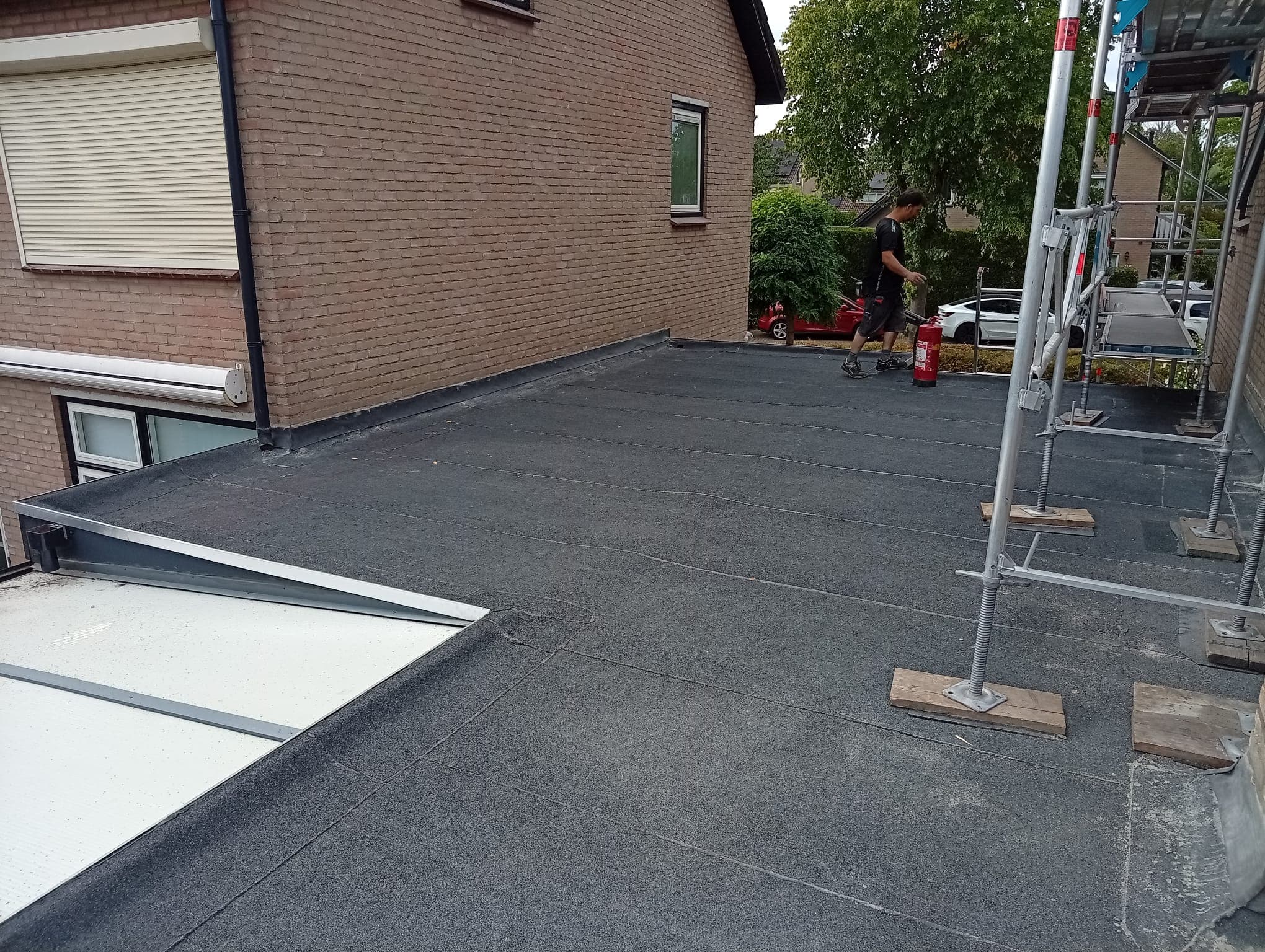 Dakdekker aan het werk op een plat bitumen dak met steiger